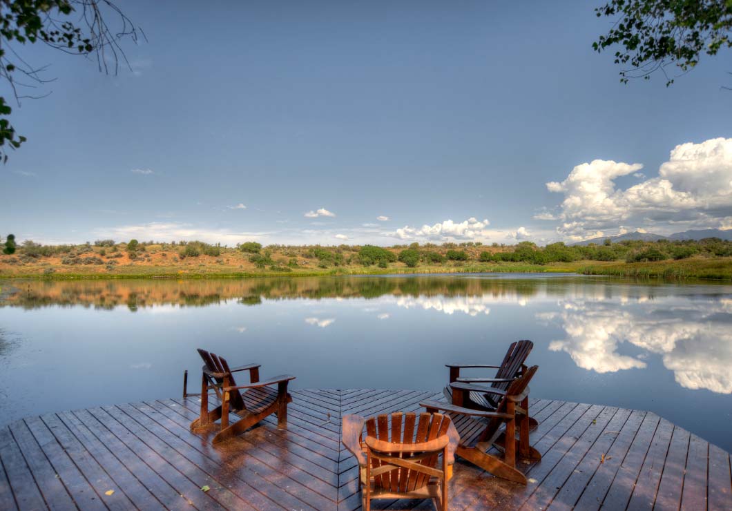 Wooden dock with three chairs overlooking a large private lake