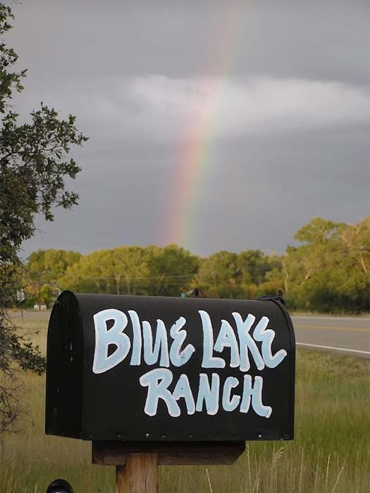 A mailbox with Blue Lake Ranch painted on it and a rainbow in the background in Durango, CO